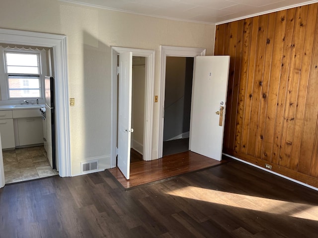 unfurnished bedroom with sink, crown molding, wooden walls, connected bathroom, and dark hardwood / wood-style flooring