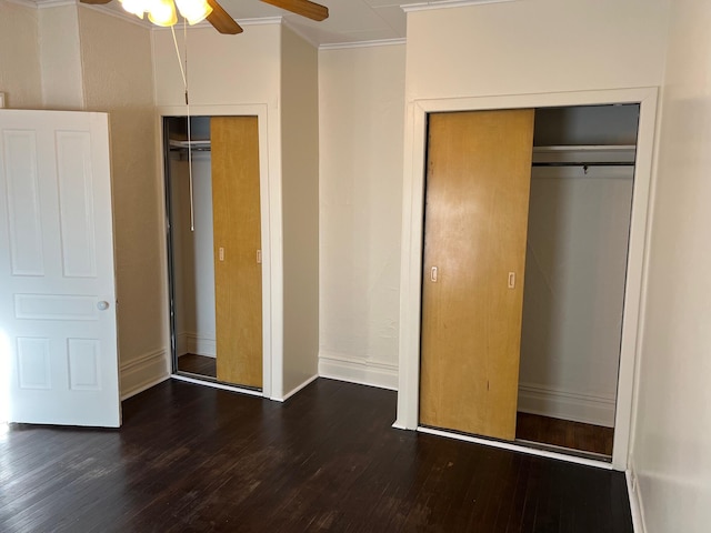 unfurnished bedroom featuring multiple closets, dark hardwood / wood-style floors, ceiling fan, and ornamental molding