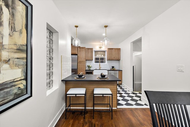 kitchen featuring dark wood-type flooring, backsplash, stainless steel fridge, decorative light fixtures, and a breakfast bar area