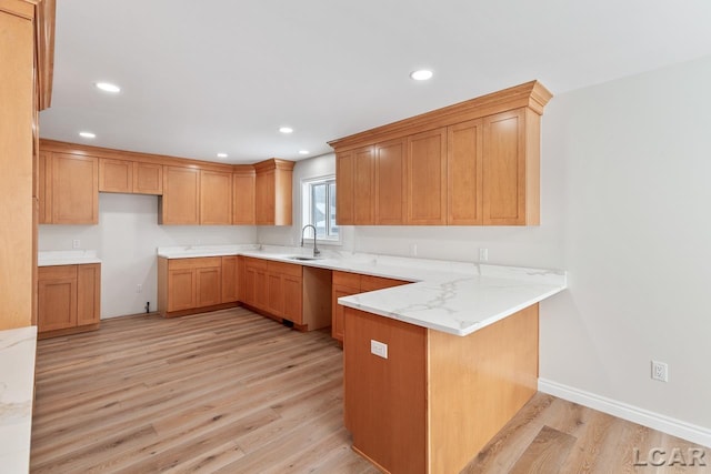 kitchen with kitchen peninsula, light hardwood / wood-style flooring, light stone counters, and sink