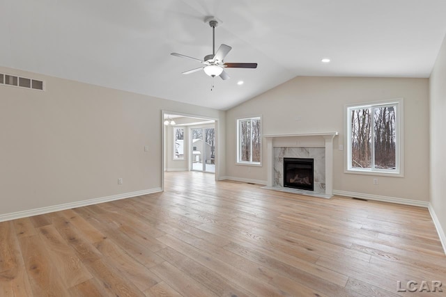 unfurnished living room with ceiling fan, vaulted ceiling, a high end fireplace, and light hardwood / wood-style flooring