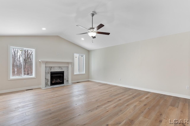 unfurnished living room with light wood-type flooring, a premium fireplace, lofted ceiling, and ceiling fan