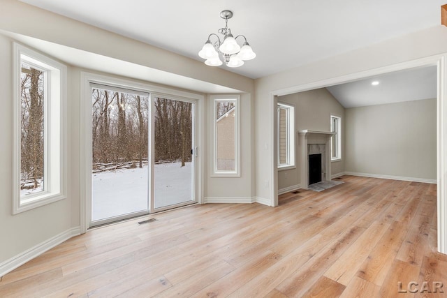 unfurnished living room with an inviting chandelier, lofted ceiling, and light hardwood / wood-style floors