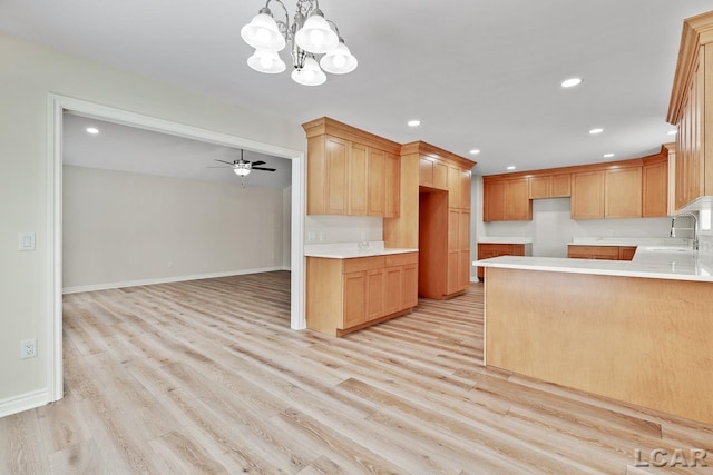 kitchen featuring kitchen peninsula, hanging light fixtures, ceiling fan with notable chandelier, light hardwood / wood-style flooring, and sink