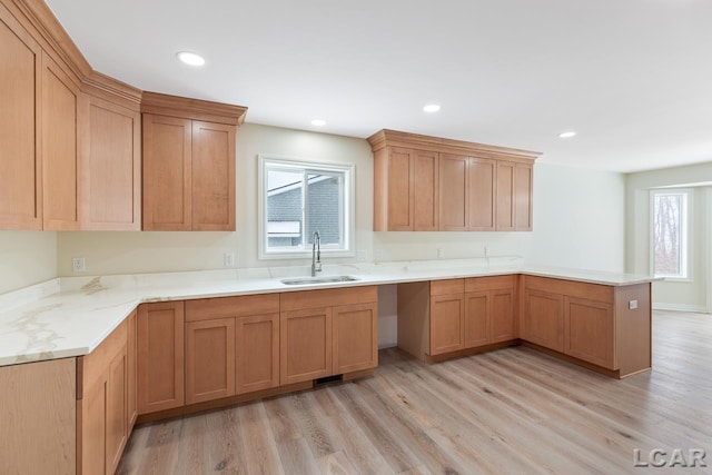 kitchen with light wood-type flooring, a wealth of natural light, kitchen peninsula, and sink