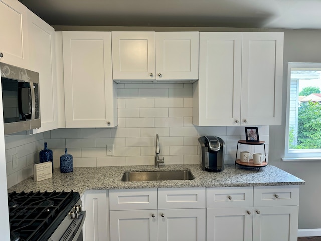 kitchen with white cabinets, sink, appliances with stainless steel finishes, tasteful backsplash, and light stone counters