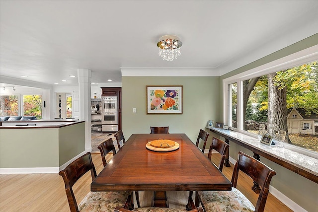 dining space with light wood-type flooring, an inviting chandelier, crown molding, and ornate columns