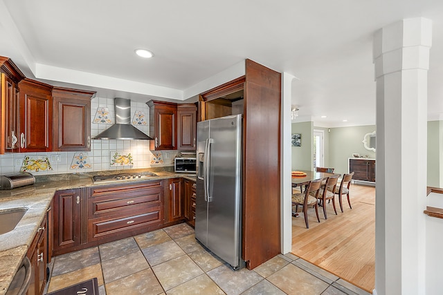 kitchen featuring wall chimney exhaust hood, stainless steel appliances, light stone counters, backsplash, and light wood-type flooring