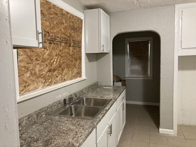 kitchen with light tile patterned flooring, a textured ceiling, white cabinetry, and sink