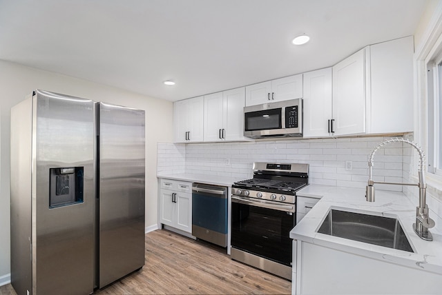 kitchen with white cabinets, light wood-type flooring, stainless steel appliances, and tasteful backsplash