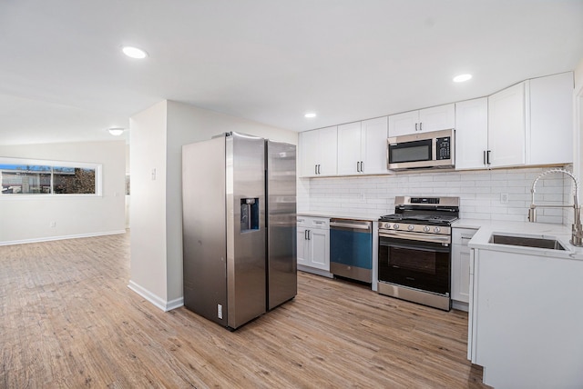 kitchen featuring white cabinets, sink, light hardwood / wood-style flooring, tasteful backsplash, and stainless steel appliances