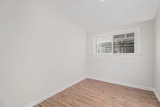 spare room featuring light wood-type flooring and vaulted ceiling