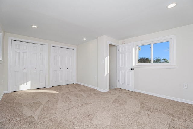 unfurnished bedroom featuring light carpet and two closets