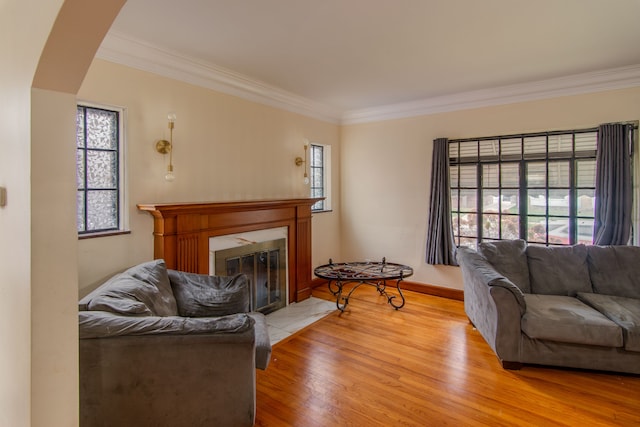 living room featuring light hardwood / wood-style flooring, crown molding, and a tiled fireplace