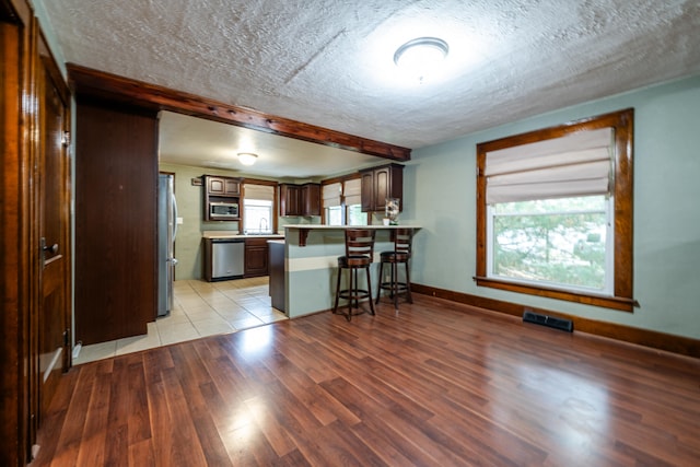 kitchen featuring a kitchen breakfast bar, light hardwood / wood-style flooring, a textured ceiling, appliances with stainless steel finishes, and kitchen peninsula