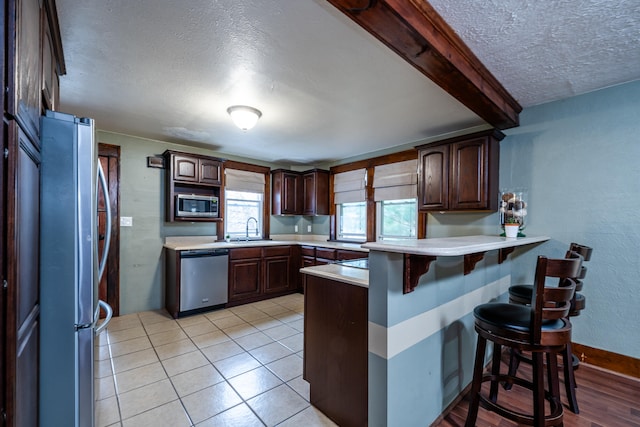 kitchen featuring sink, stainless steel appliances, a kitchen breakfast bar, kitchen peninsula, and a textured ceiling