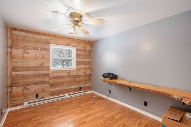 spare room featuring ceiling fan, baseboard heating, built in desk, hardwood / wood-style floors, and wood walls