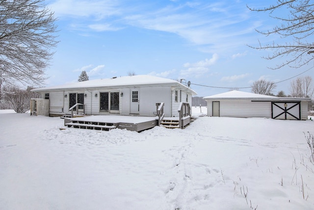 snow covered property featuring an outbuilding, a deck, and a garage