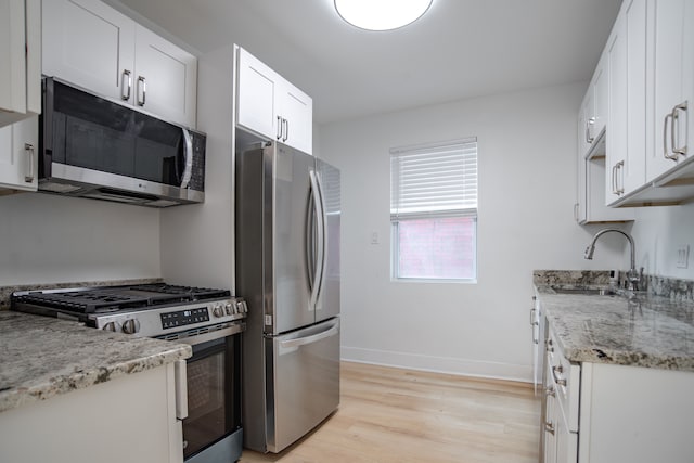 kitchen featuring light stone countertops, sink, white cabinets, light hardwood / wood-style flooring, and stainless steel appliances