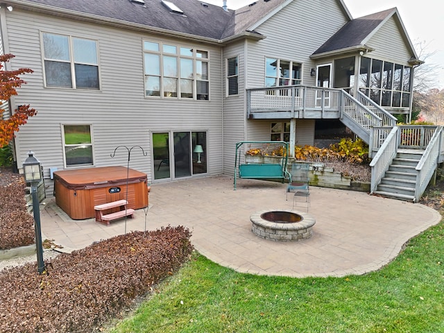 back of property with a sunroom, a wooden deck, a patio area, an outdoor fire pit, and a hot tub