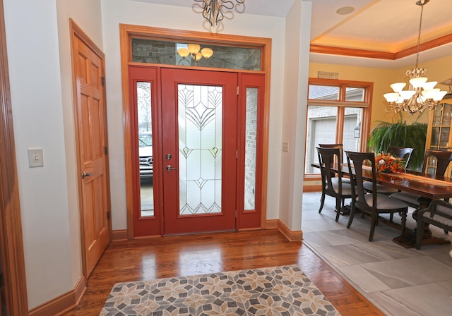 foyer entrance with a raised ceiling, dark hardwood / wood-style floors, and a notable chandelier