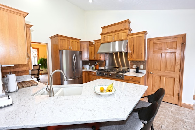 kitchen with a breakfast bar, high vaulted ceiling, sink, range hood, and stainless steel refrigerator