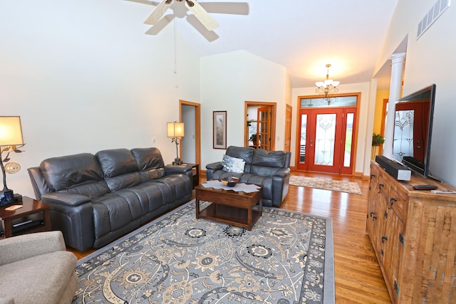 living room featuring ceiling fan with notable chandelier, ornate columns, high vaulted ceiling, and light hardwood / wood-style flooring