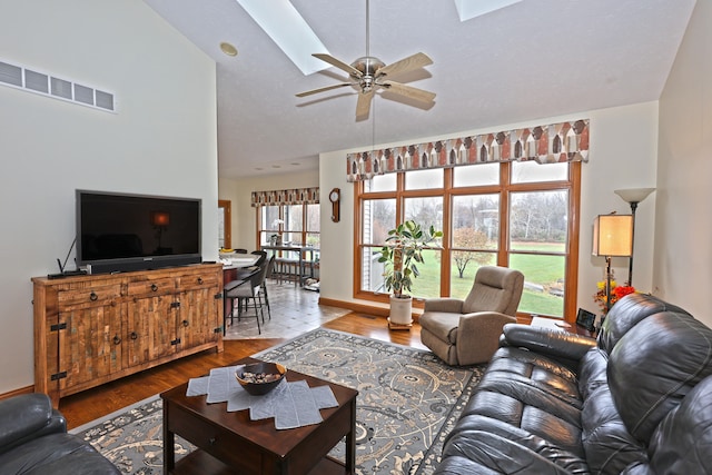 living room featuring hardwood / wood-style floors, ceiling fan, and vaulted ceiling with skylight