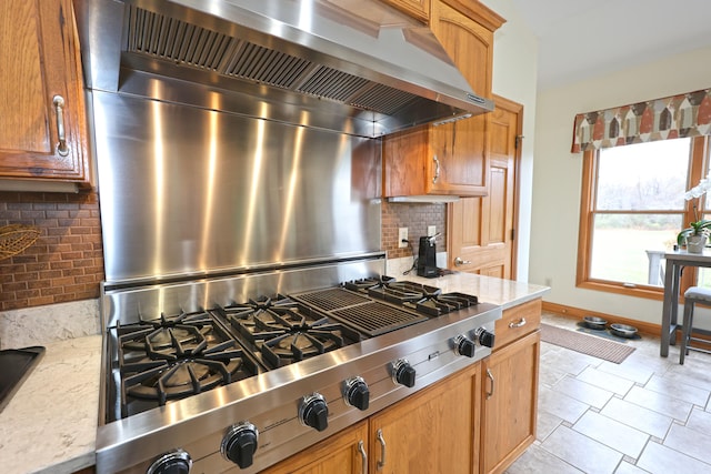 kitchen featuring backsplash, light stone countertops, wall chimney range hood, and stainless steel gas cooktop