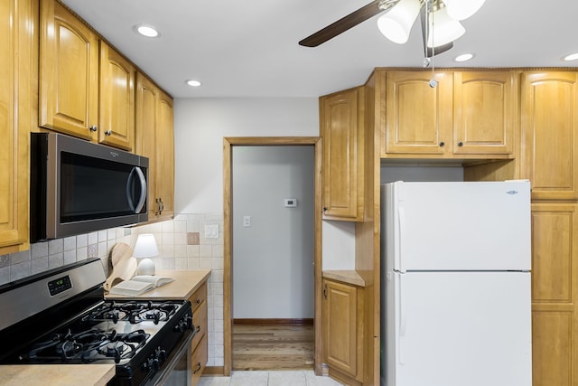 kitchen featuring appliances with stainless steel finishes, light wood-type flooring, ceiling fan, and backsplash