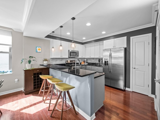 kitchen featuring kitchen peninsula, a kitchen bar, dark hardwood / wood-style flooring, stainless steel appliances, and white cabinets