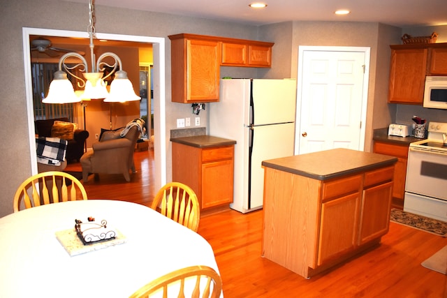 kitchen with a kitchen island, an inviting chandelier, white appliances, and light hardwood / wood-style flooring