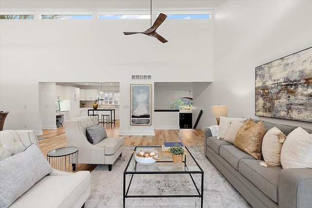 living room featuring ceiling fan, light hardwood / wood-style floors, and a towering ceiling