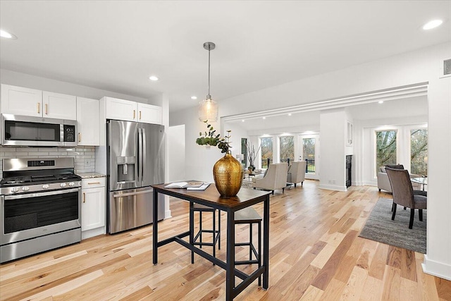 kitchen with backsplash, appliances with stainless steel finishes, decorative light fixtures, light hardwood / wood-style floors, and white cabinetry