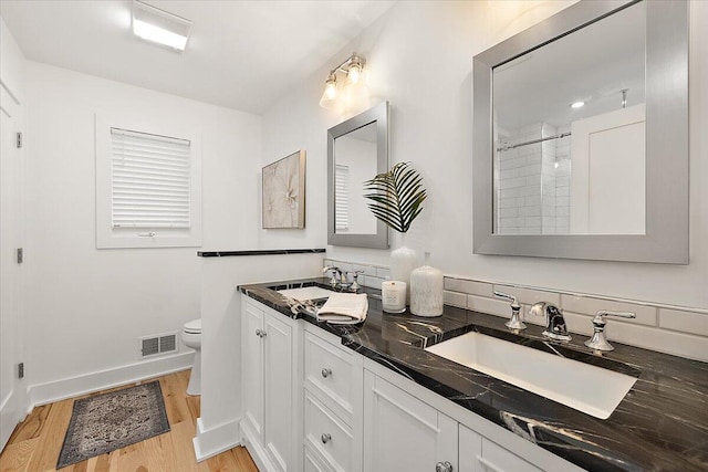 bathroom featuring a tile shower, vanity, wood-type flooring, and toilet