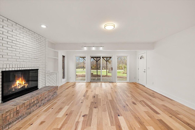 unfurnished living room featuring light wood-type flooring and a brick fireplace