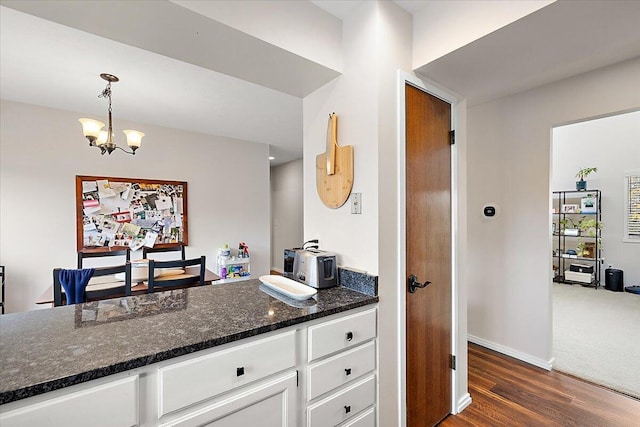 kitchen with dark wood-type flooring, hanging light fixtures, dark stone countertops, a notable chandelier, and white cabinetry