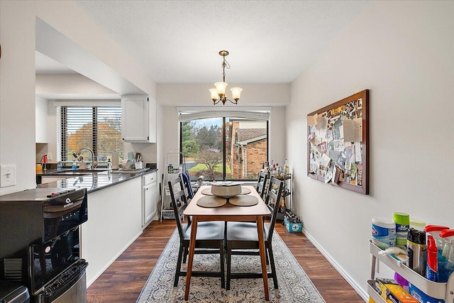 dining space featuring a textured ceiling, a notable chandelier, sink, and dark wood-type flooring