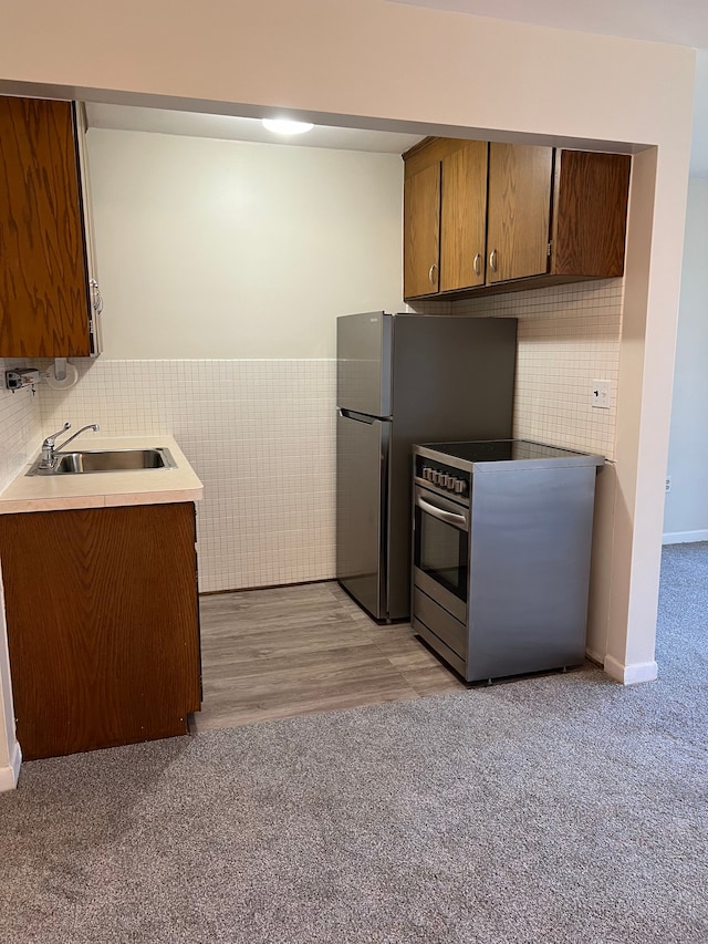 kitchen featuring sink, light wood-type flooring, tile walls, and appliances with stainless steel finishes