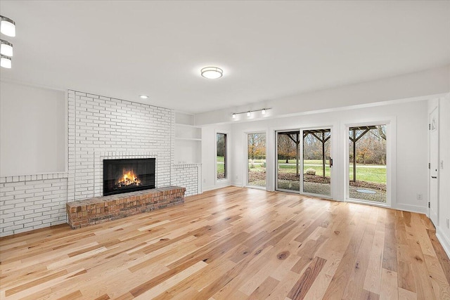 unfurnished living room featuring built in shelves, light wood-type flooring, a brick fireplace, and brick wall