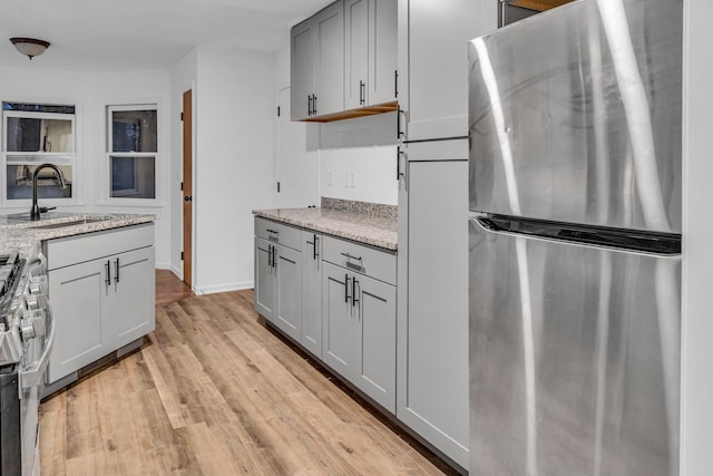 kitchen with gray cabinetry, backsplash, sink, appliances with stainless steel finishes, and light stone counters