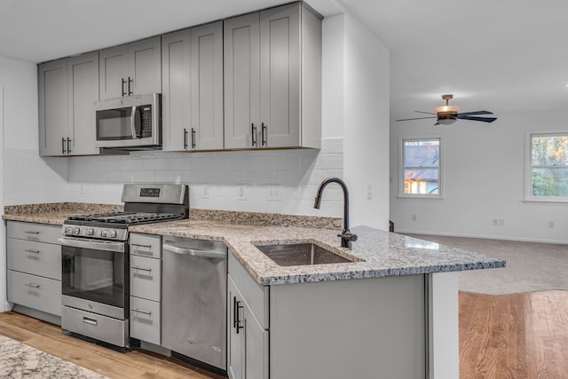 kitchen with light stone countertops, sink, ceiling fan, stainless steel appliances, and decorative backsplash