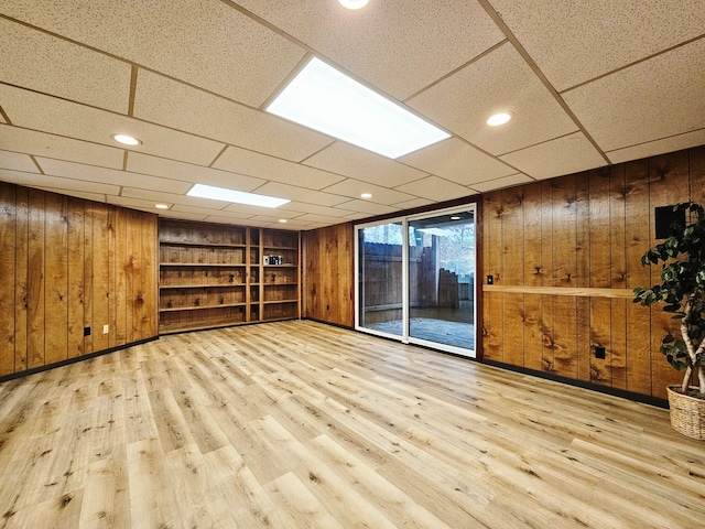 interior space featuring a paneled ceiling, built in shelves, light wood-type flooring, and wooden walls