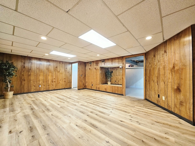 basement with a paneled ceiling, wooden walls, and light hardwood / wood-style flooring