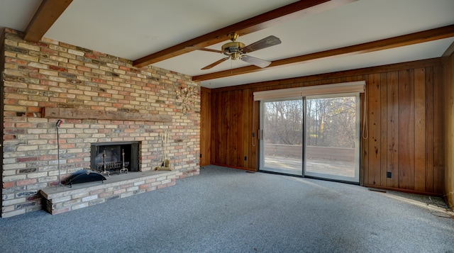 unfurnished living room featuring wooden walls, a fireplace, beamed ceiling, and light carpet