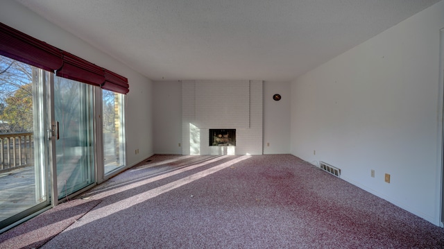 unfurnished living room with carpet flooring, a textured ceiling, and a brick fireplace