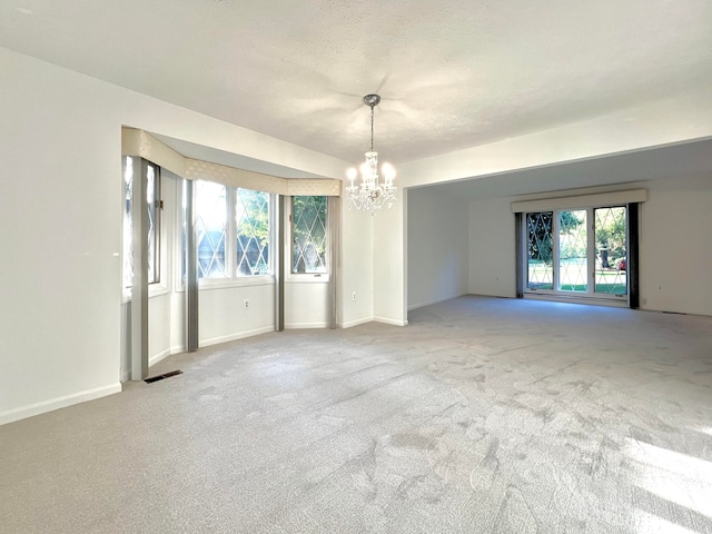 carpeted spare room featuring a textured ceiling, a wealth of natural light, and a notable chandelier