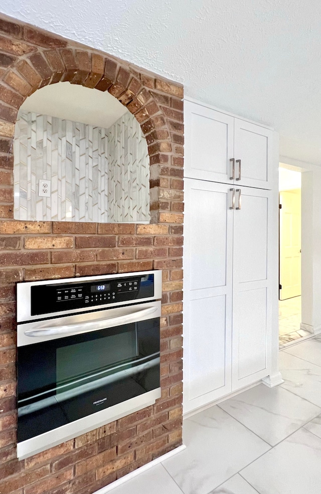 kitchen featuring stainless steel oven, white cabinetry, and a textured ceiling