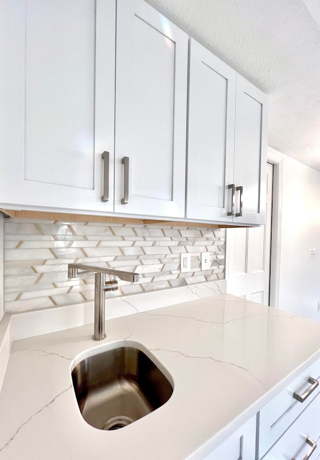 kitchen featuring decorative backsplash, light stone counters, sink, and white cabinets