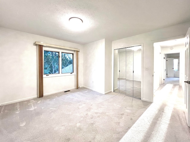 unfurnished bedroom featuring light carpet, a closet, and a textured ceiling